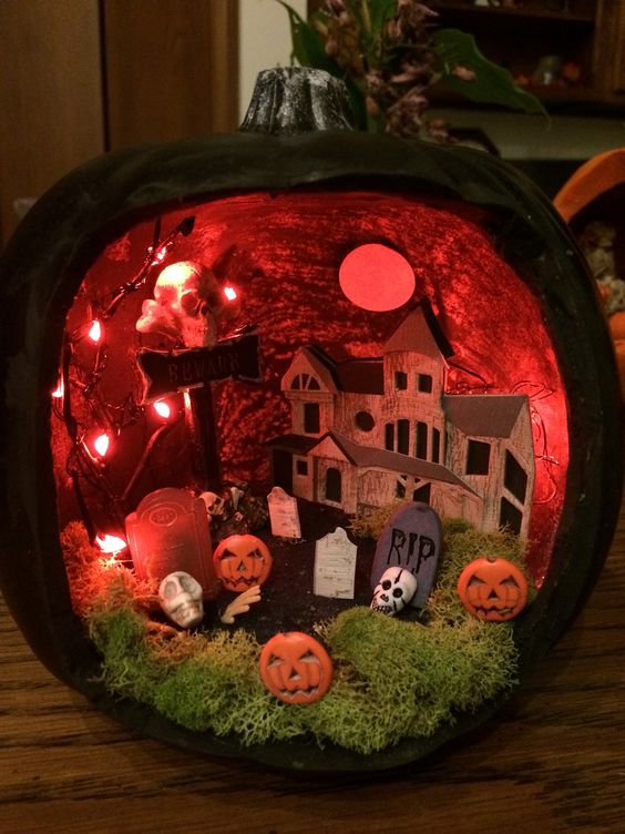 a black pumpkin diorama with red lights and a paper house, a moss graveyard and pumpkins plus a red moon