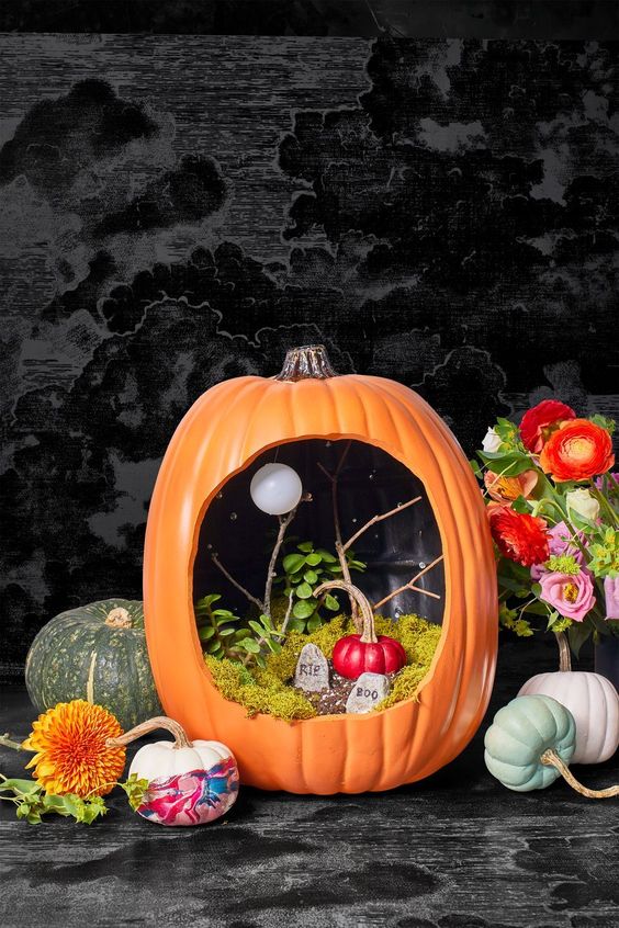 a simple and bright Halloween pumpkin with moss, tombstones, greenery and branches plus a red pumpkin inside it is fun