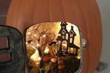 a small Halloween pumpkin diorama with a black painted house, a black tree with lights, moss, pumpkins and bats