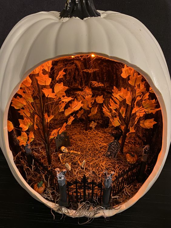 a white Halloween diorama with a graveyard with skeletons, pumpkins and fall trees plus lights over the space is amazing