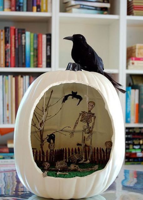 a white Halloween diorama with grass, a fence, skeletons and a tree plus a blackbird on top is a lovely idea for styling your party