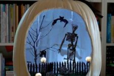 a white Halloween pumpkin with a black skeleton, a tree, a fence, bats and a black cat, skulls and lights is amazing