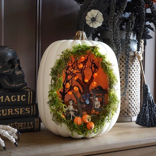 a white pumpkin decorated with grass, skeletons, trees with pumpkin lights and small pumpkins is super fun for Halloween