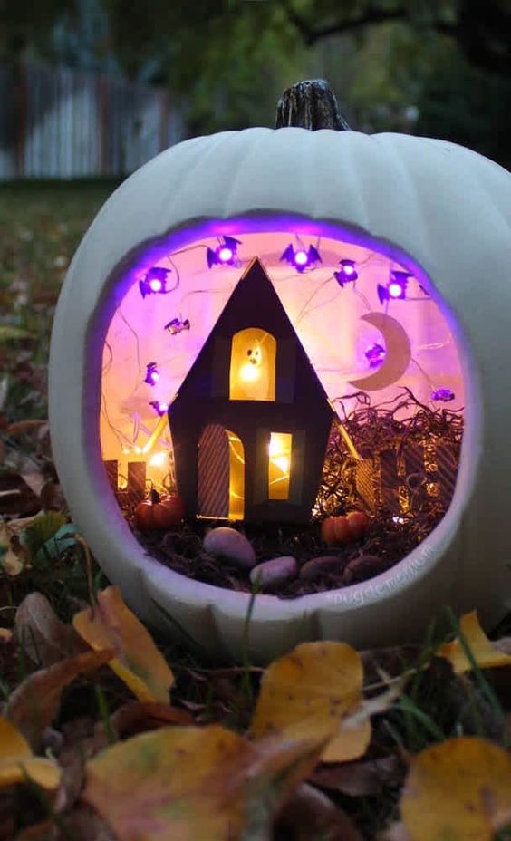 a white pumpkin diorama with purple bat lights, a black house with a ghost and a moon, with small pumpkins and hay