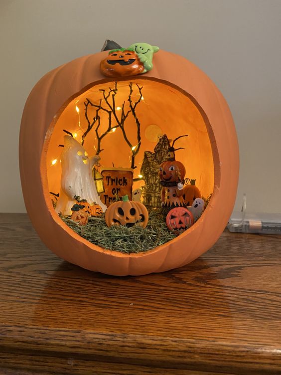 an orange Halloween pumpkin diorama with hat, mini pumpkins, ghosts, lights and branches is a lovely decoration for a kids' party