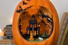 an orange pumpkin diorama with a black house, a tree, a stack of pumpkins and grass and bats on the side of the pumpkin