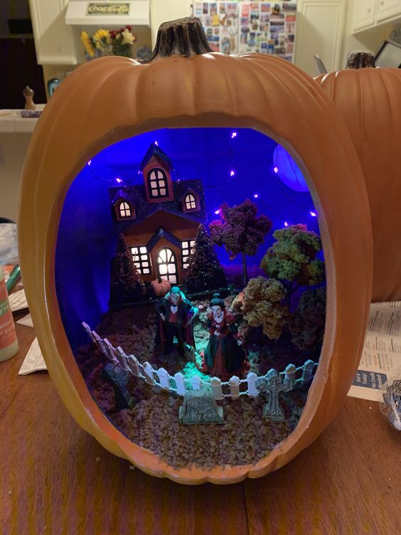 an orange pumpkin with a blue inside and lights, a black house, some witches and trees and a fence to separate the graveyard