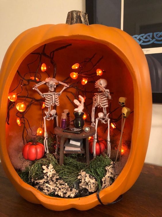an orange pumpkin with greenery and bark, pumpkins, pumpkin lights and skeletons at a table is a fun idea