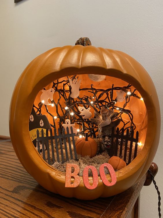 an orange pumpkin with hay, a fence, a paper house, ghosts attached to the lights and small pumpkins
