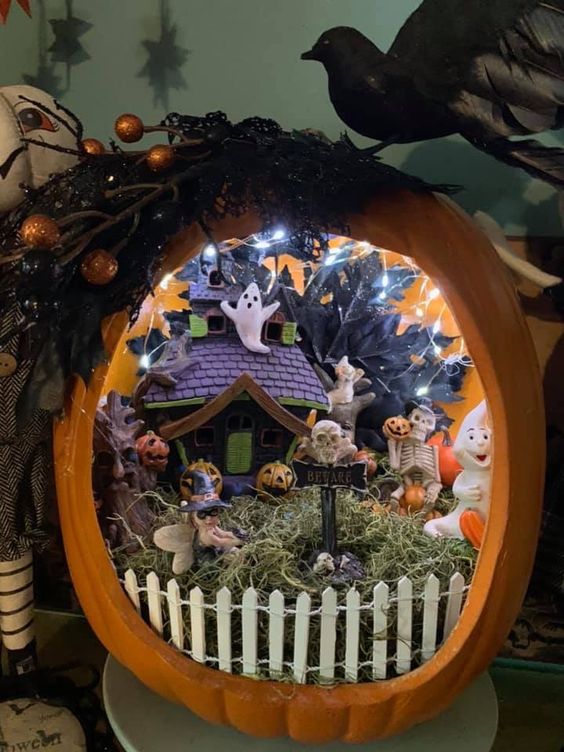 an orange pumpkin with lights, ghosts, jack o lanterns, hay and a fence plus a purple and green little house for Halloween