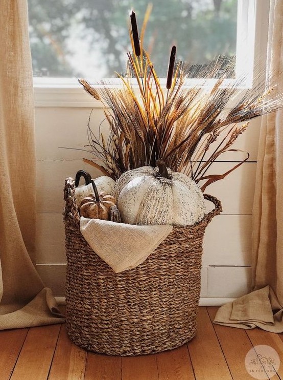 a boho Thanksgiving decoration of a basket with faux pumpkins, some grasses and wheat is a cool and cozy solution