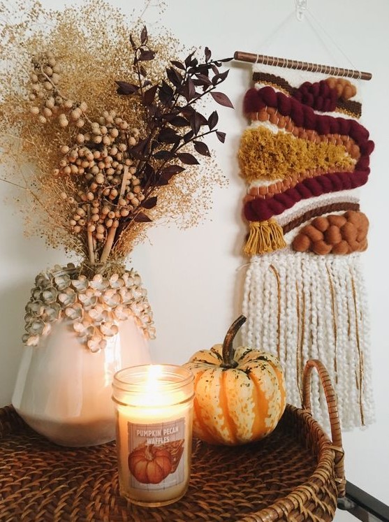 a bright fall woven hanging, a pumpkin and a candle, a vase with dried branches and berries for boho Thanksgiving decor