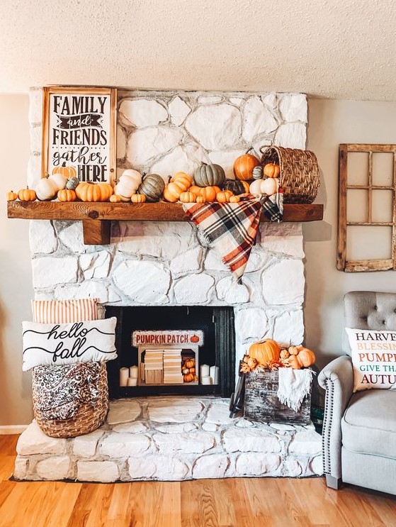 a cozy and chic Thanksgiving mantel with lots of pumpkins, a basket, a plaid blanket, a sign and some pumpkins in a crate