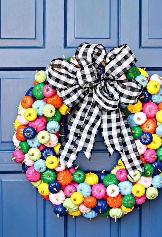 a super colorful mini pumpkin wreath with gilded stems and a black and white plaid bow on top is amazing for the fall