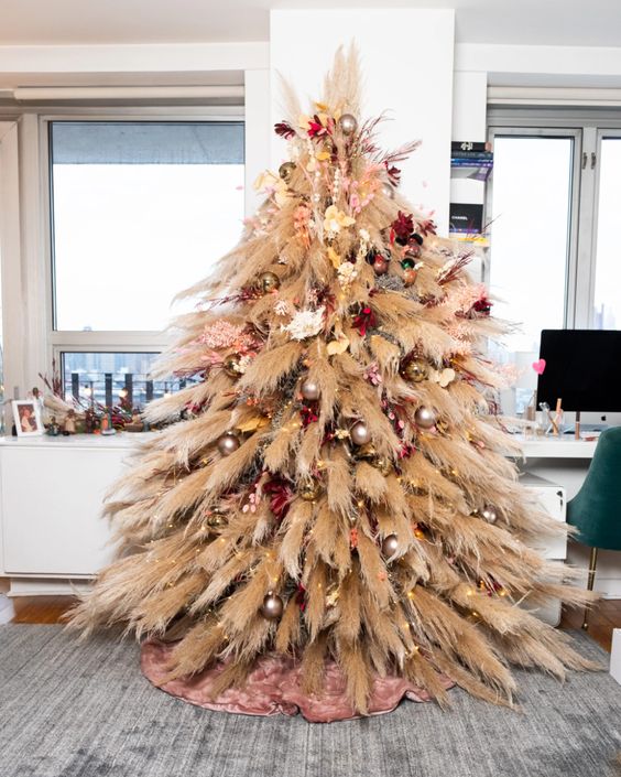 a pampas grass Christmas tree decorated with some metallic ornaments, bright blooms and lights is a bold boho decor idea
