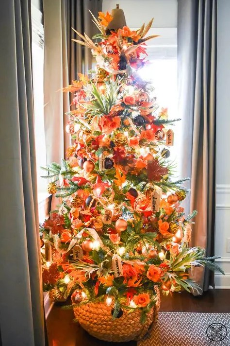 a gorgeous bright Thanksgiving tree with lights, ornage, gold and black ornaments, faux leaves, foliage and a pumpkin on top