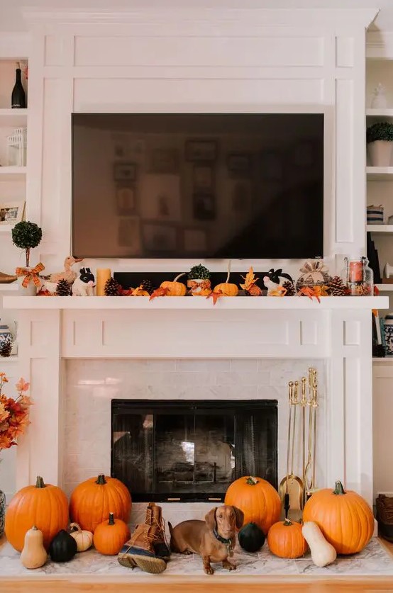 a lovely Thanksgiving mantel with bold leaves, candles, pinecones, small pumpkins on the mantel and larger ones next to the fireplace