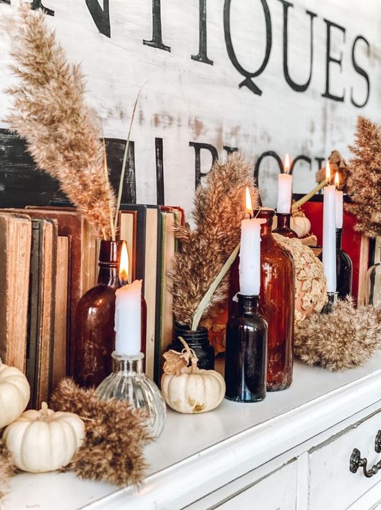 boho Thanksgiving decor with neutral pumpkins and dried blooms, white candles in dark apothecary bottles and vintage books