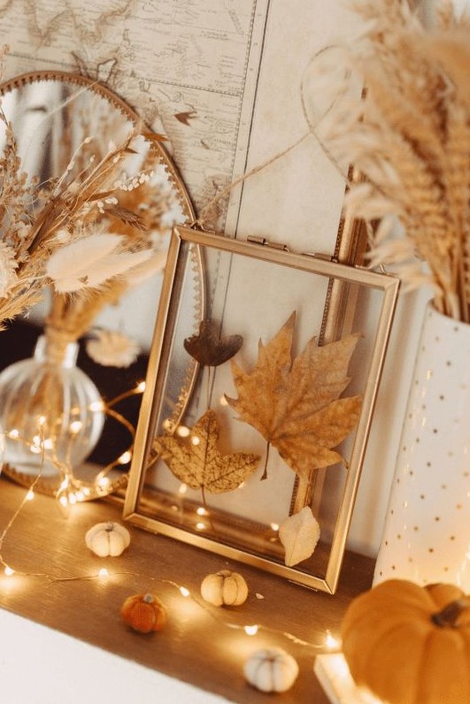 lovely boho Thanksgiving decor with little pumpkins, lights, grasses and wheat and pressed leaves in a frame