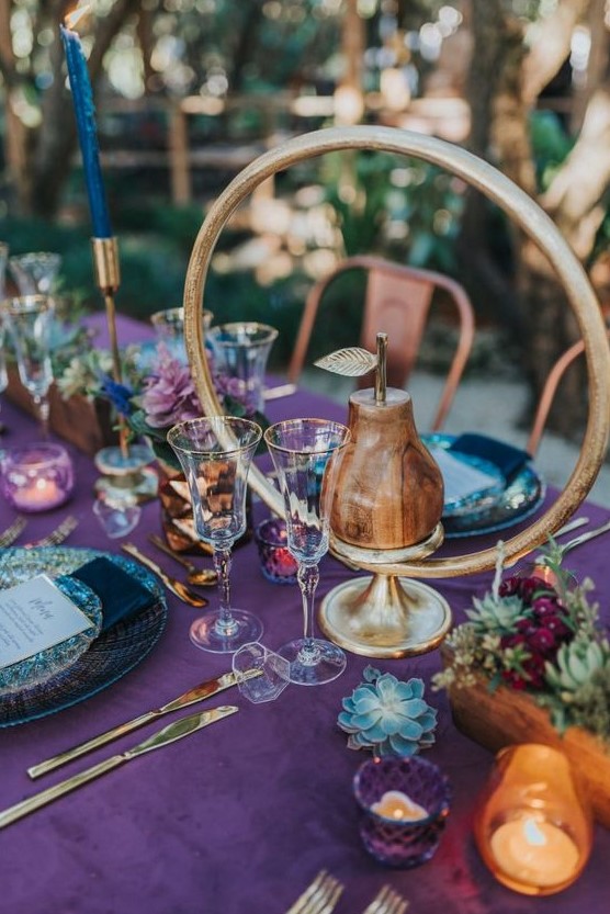 a beautiful Thanksigiving tablescape with a purple tablecloth, chic plates, succulents and greenery, navy candles