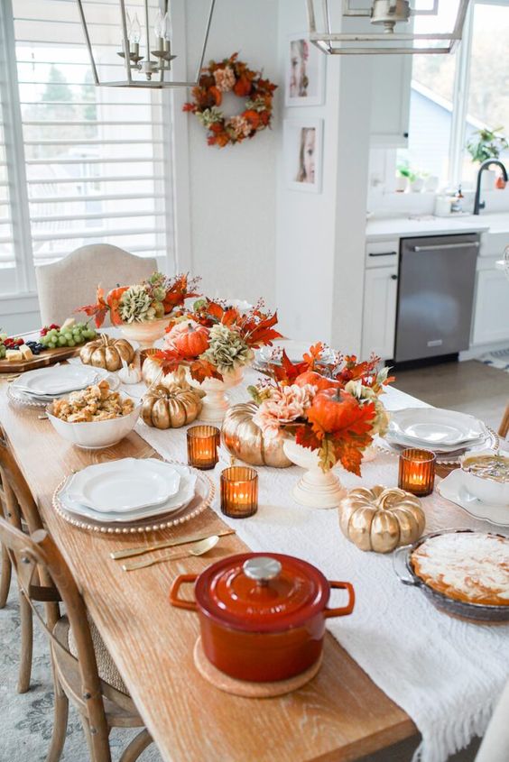 a bold Thanksgiving table setting with bright fall leaves and gilded pumpkins, amber candleholders and white porcelain