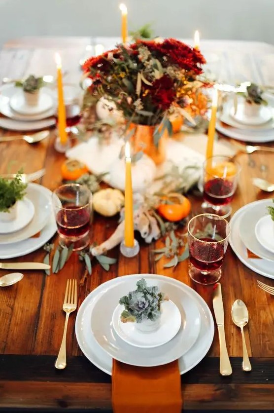 a bold rustic Thanksgiving table with rust napkins, pumpkins, greenery, a bold floral arrangement and bright candles