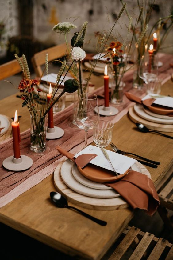 a beautiful Thanksgiving table setting with a rust-colored runner and napkins, wood slice placemats, rust candles and dried blooms