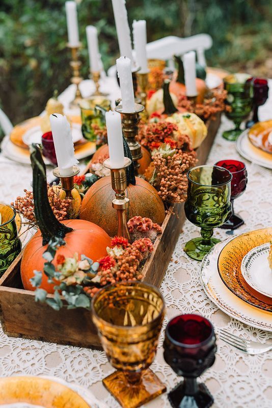 a bold Thanksgiving tablescape with orange pumpkins and berries, green, amber and burgundy glasses and tall and thin candles