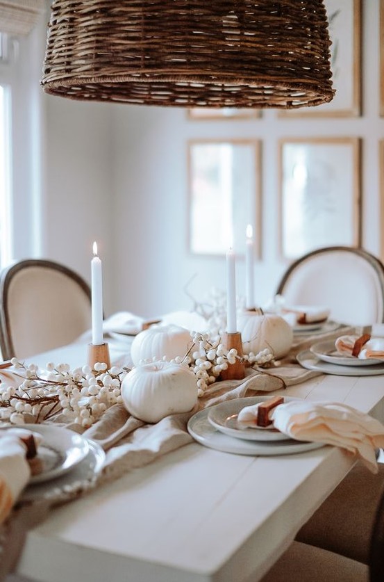 a beautiful Thanksgiving tablescape with white candles and pumpkins, grey plates and neutral linens, wooden candleholders and berries