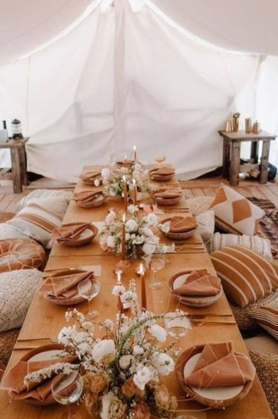 a boho thanksgiving feast space with terracotta linens, white blooms and rust candles plus lots of pillows