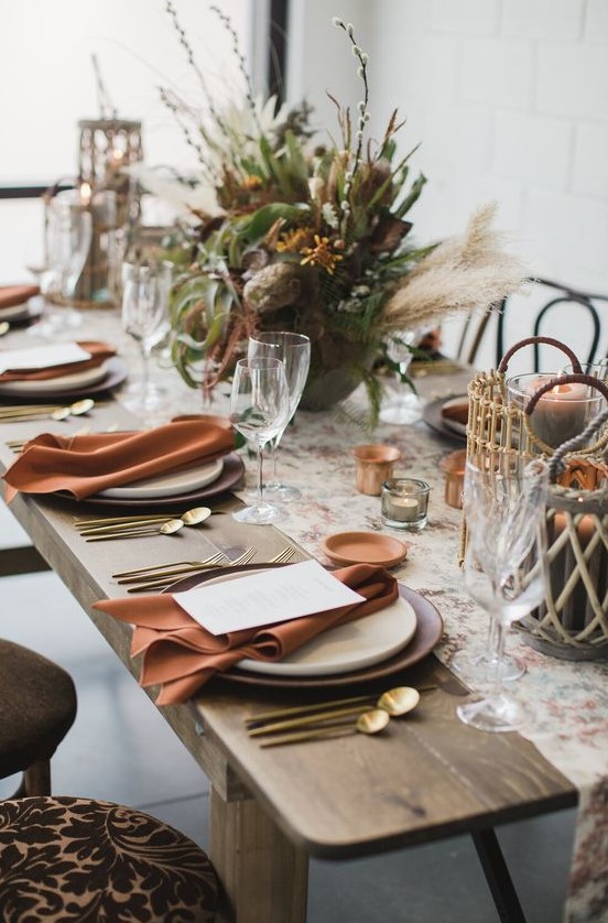 a boho Thanksgiving table setting with a lush greenery, pampas grass and willow, rust napkins and gold cutlery