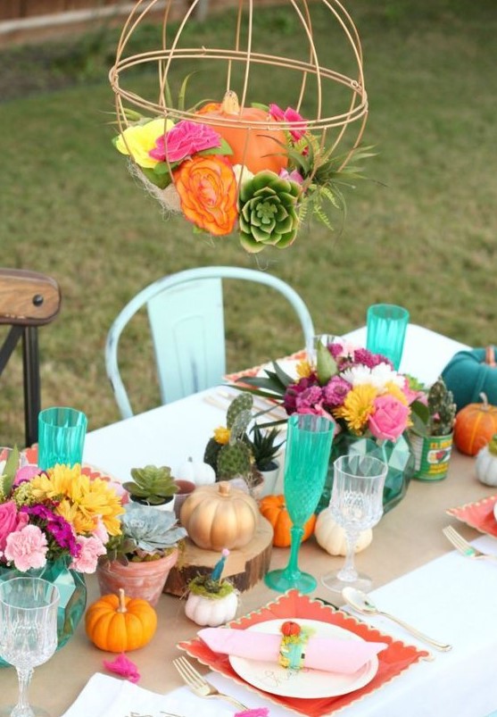 a bright Friendsgiving tablescape with colroful blooms, pumpkins, succulents and cacti, a cage with blooms and a pumpkin