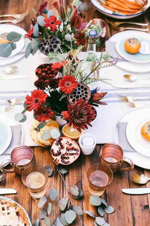 a bright boho Thanksgiving tablescape with neutral printed linens, bold blooms and lotus slices, greenery and copper mugs
