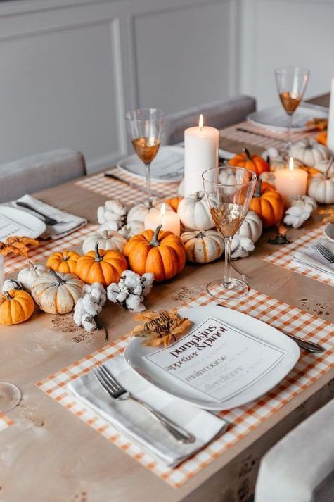 a bright rustic Thanksgiving tablescape with white and orange pumpkins, pillar candles, plaid placemats and leaves