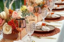 26 a colorful boho Thanksgiving tablescape with a yellow runner, bright blooms and grasses, orange woven placemats and copper glasses
