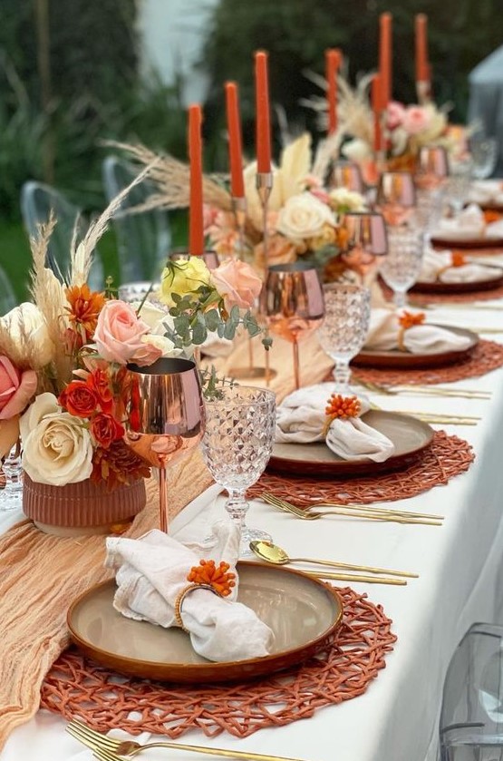 a colorful boho Thanksgiving tablescape with a yellow runner, bright blooms and grasses, orange woven placemats and copper glasses