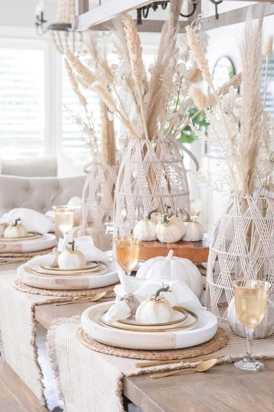 a cool rustic meets boho Thanksgiving tablescape with pampas grass in yarn covered vases, white faux pumpkins, large wooden chargers and woven placemats