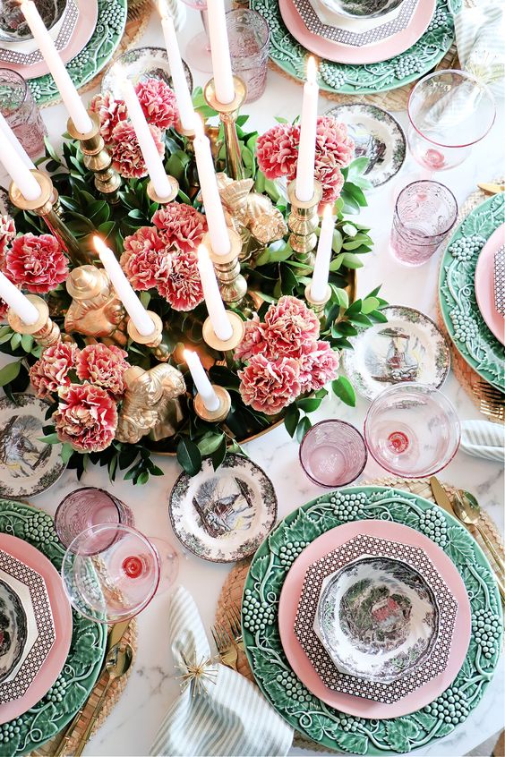 a colorful Thanksgiving table setting with pink and green plates, pink blooms and greenery, lots of candles and pink glasses