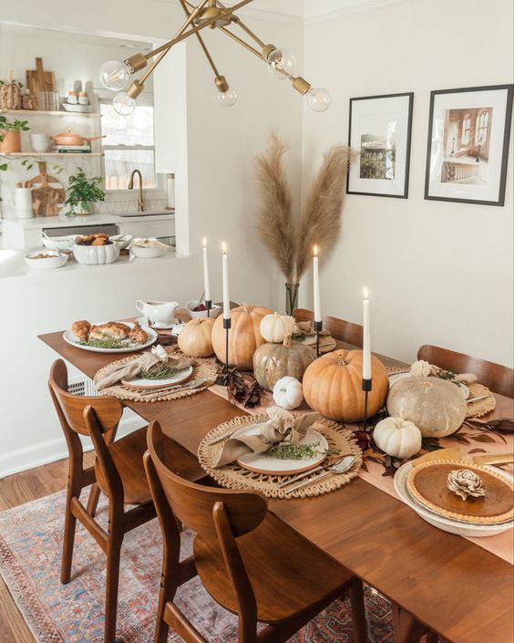 a cozy boho Thanksgiving table with neutral pumpkins, white candles, woven placemats, neutral napkins and gold cutlery