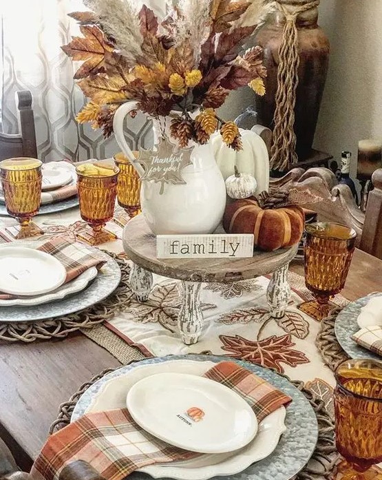 a cozy rustic Thanksgiving tablescape with an embroidered table runner and rust plaid napkins, a stand with faux pumpkins, leaves and pinecones