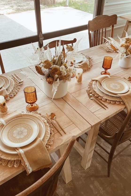 a cozy boho Thanksgiving tablescape with woven placemats, printed plates, warm-colored napkins and lovely dried flower centerpieces