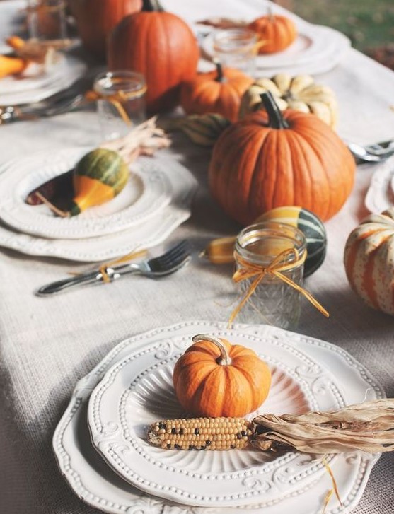 a natural tablescape with pumpkins, corn cobs, husks, candles and some elegant vintage plates