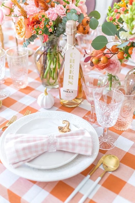 a cool blush and orange Thanksgiving tablscape with orange and pink blooms, white pumpkins and gold cutlery