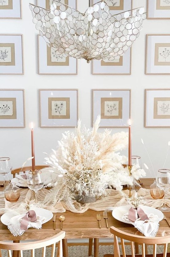 a lovely boho Thanksgiving table setting with a lush dried bloom and grass centerpiece, white porcelain, orange candles and matte cutlery