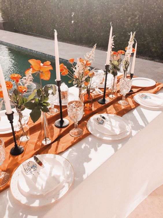 a pretty Thanksgiving table setting with a rust table runner, rust blooms and dried grasses, candles and white plates