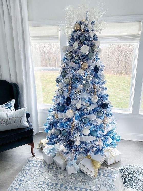 an icy blue Christmas tree decorated with pale and navy ornaments, white, gold and silver ones plus frosted branches with pompoms on its top is a creative idea