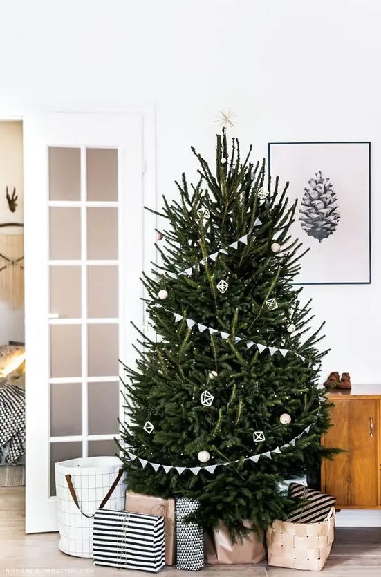 a modern Scandi tree with buntings, white and wooden ornaments and a star on top plus lights