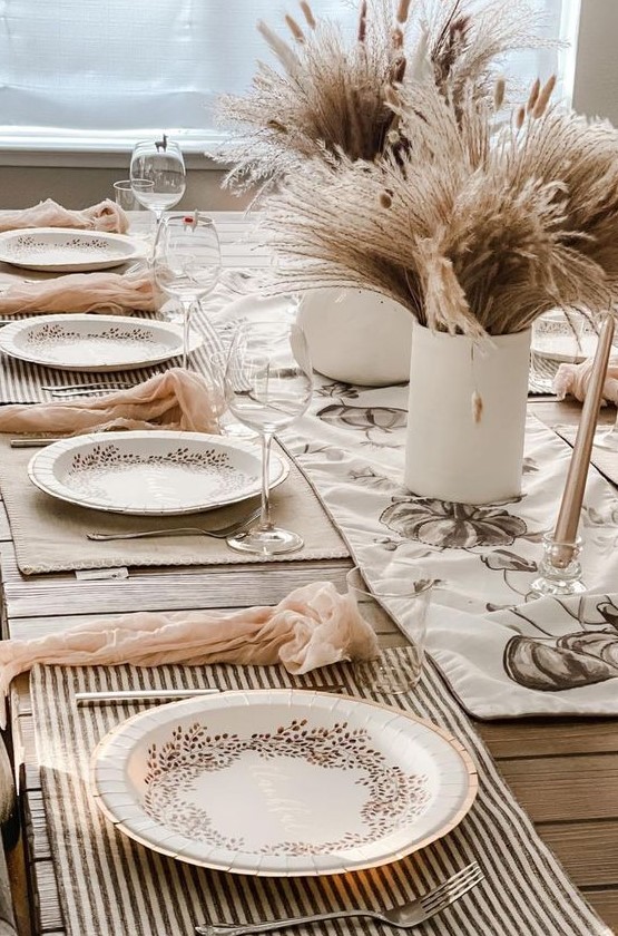 a neutral boho Thanksgiving tablescape with wheat and grass centerpieces, striped placemats, blush napkins and printed plates