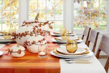 32 a pretty Thanksgiving tablescape with an orange plaid table runner and berries covering the pumpkins, amber glasses and napkins