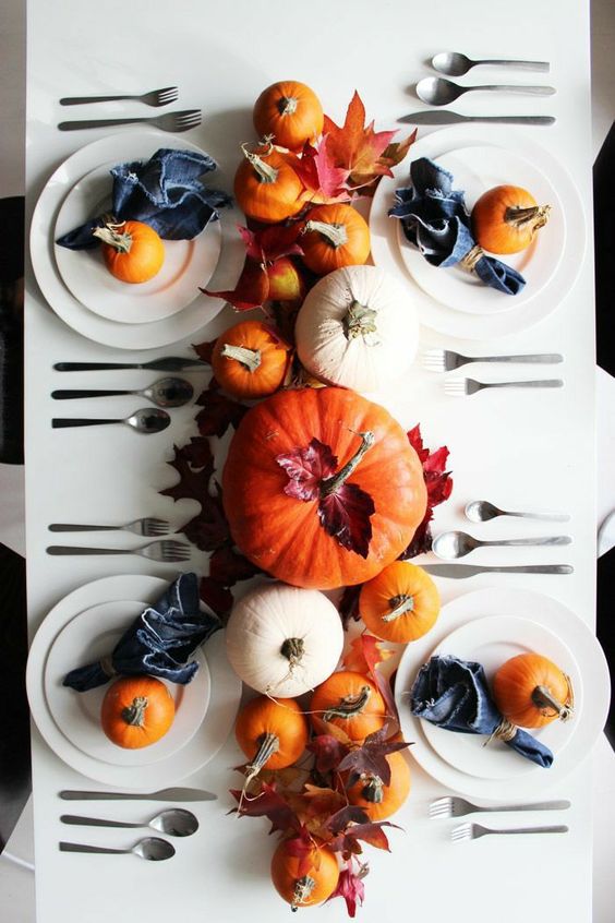 a simple and pretty modern Thanksgiving tablescape with white plates, white and orange pumpkins, fall leaves and indigo napkins